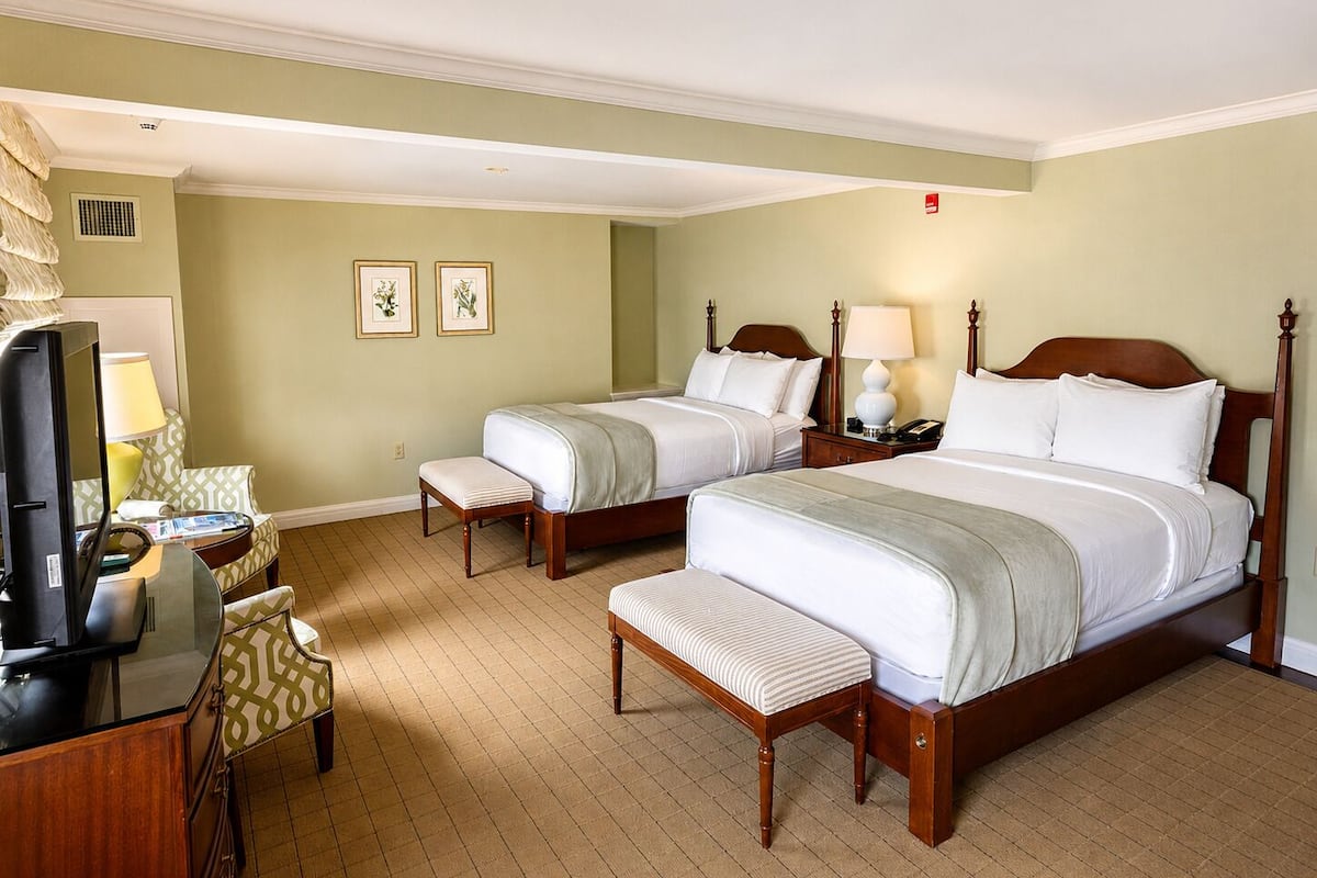 Une chambre d’hôtel avec deux lits, un bureau avec une chaise, une télévision et une petite table avec une lampe.