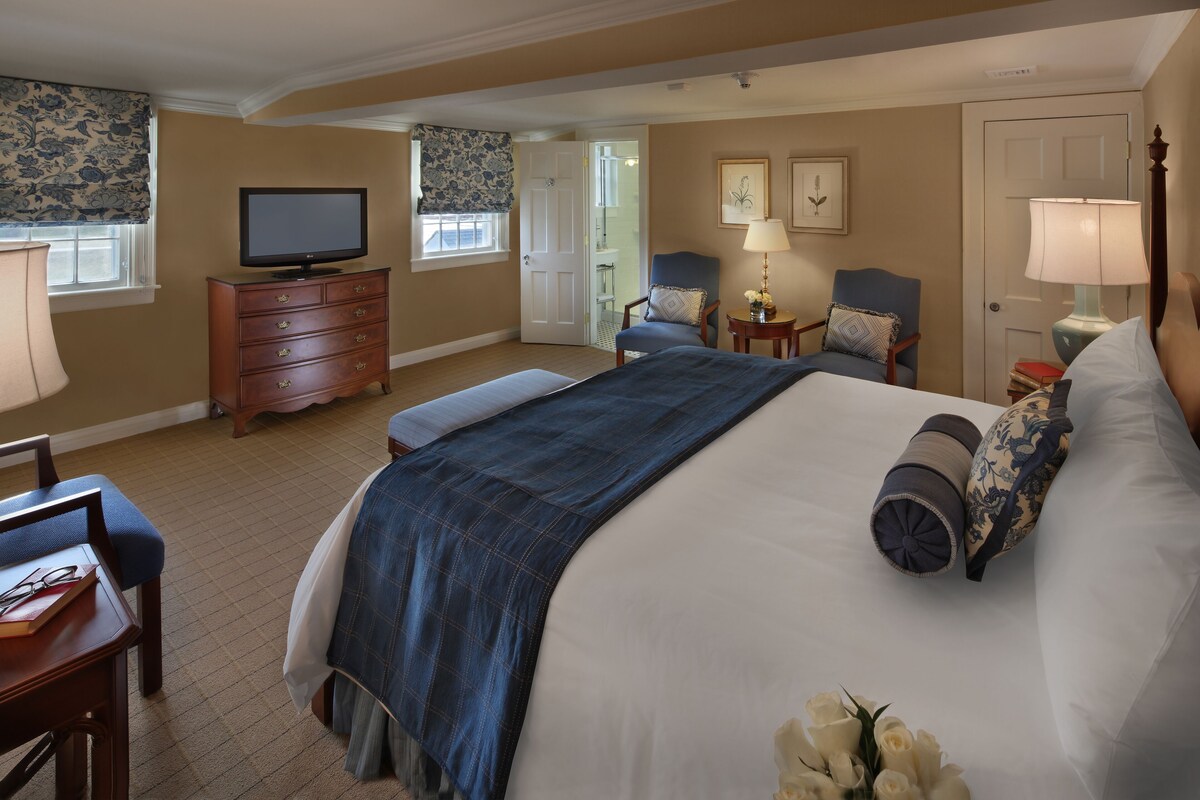 A hotel room with a large bed, a television, a desk with a chair, and a window with curtains.