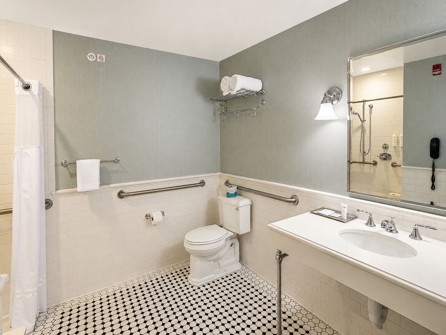 Un baño con inodoro, lavamanos, ducha y barras de apoyo.