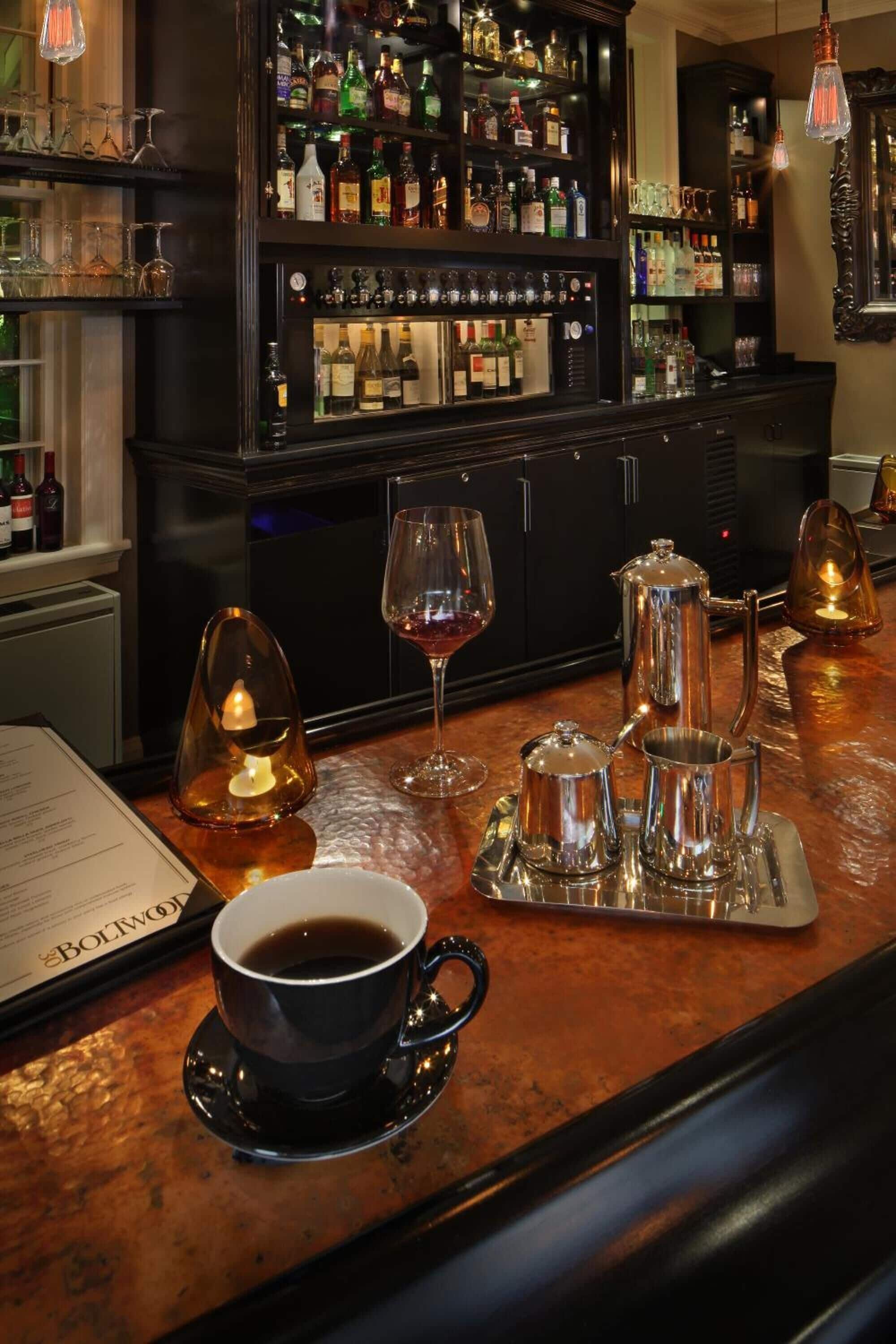 A bar area with a coffee cup, wine glass, and various bottles on shelves.