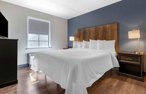 A hotel room with a large bed, a nightstand, a lamp, a window, and a television.