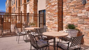 An outdoor patio with round tables and chairs, stone walls, and a metal gate. - Springhill Suites by Marriott Thatcher (Thatcher)