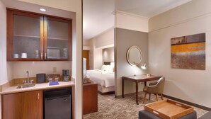 A hotel room with a kitchenette, a bed, a desk with a chair, a mirror, and a painting on the wall. - Springhill Suites by Marriott Thatcher (Thatcher)