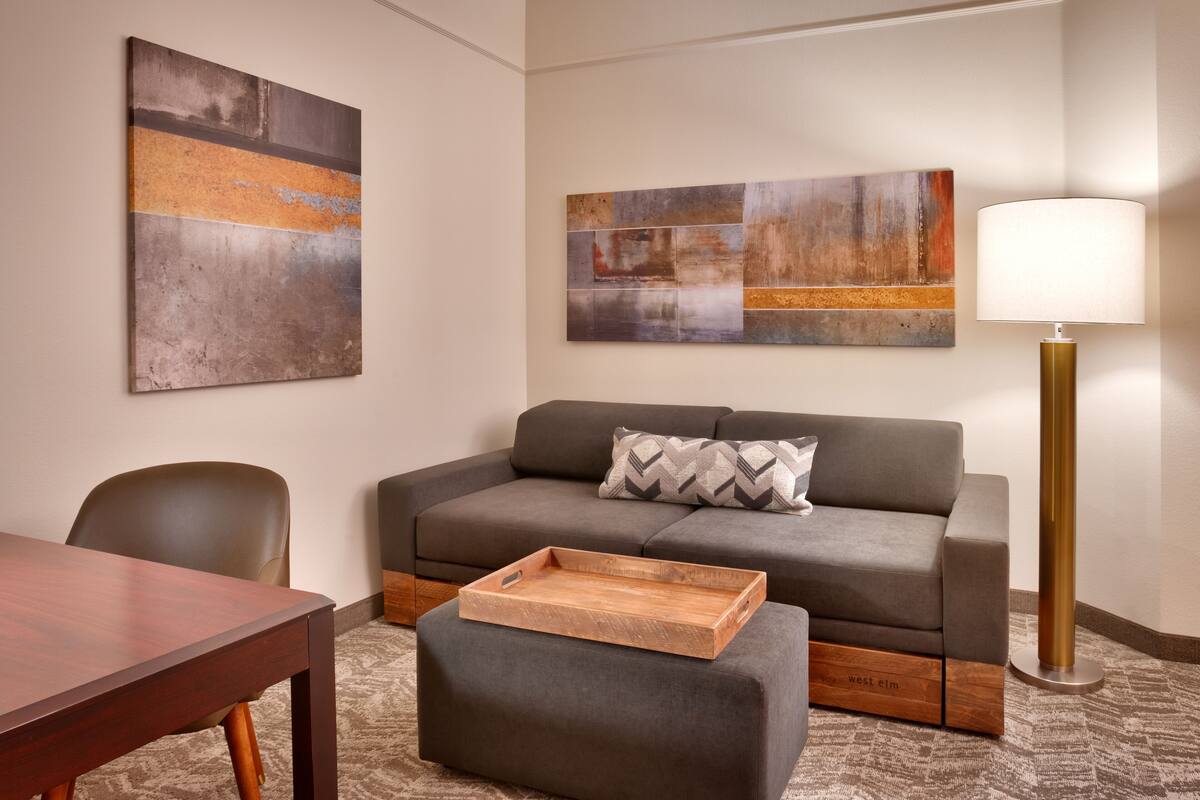 A modern living room with a grey sofa, a wooden coffee table, a lamp, and abstract wall art.