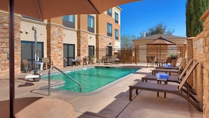 A pool area with lounge chairs and umbrellas, surrounded by stone walls and a building with multiple windows. - Springhill Suites by Marriott Thatcher (Thatcher)