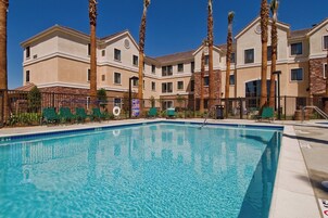Una piscina con agua cristalina azul, rodeada por una valla y palmeras.