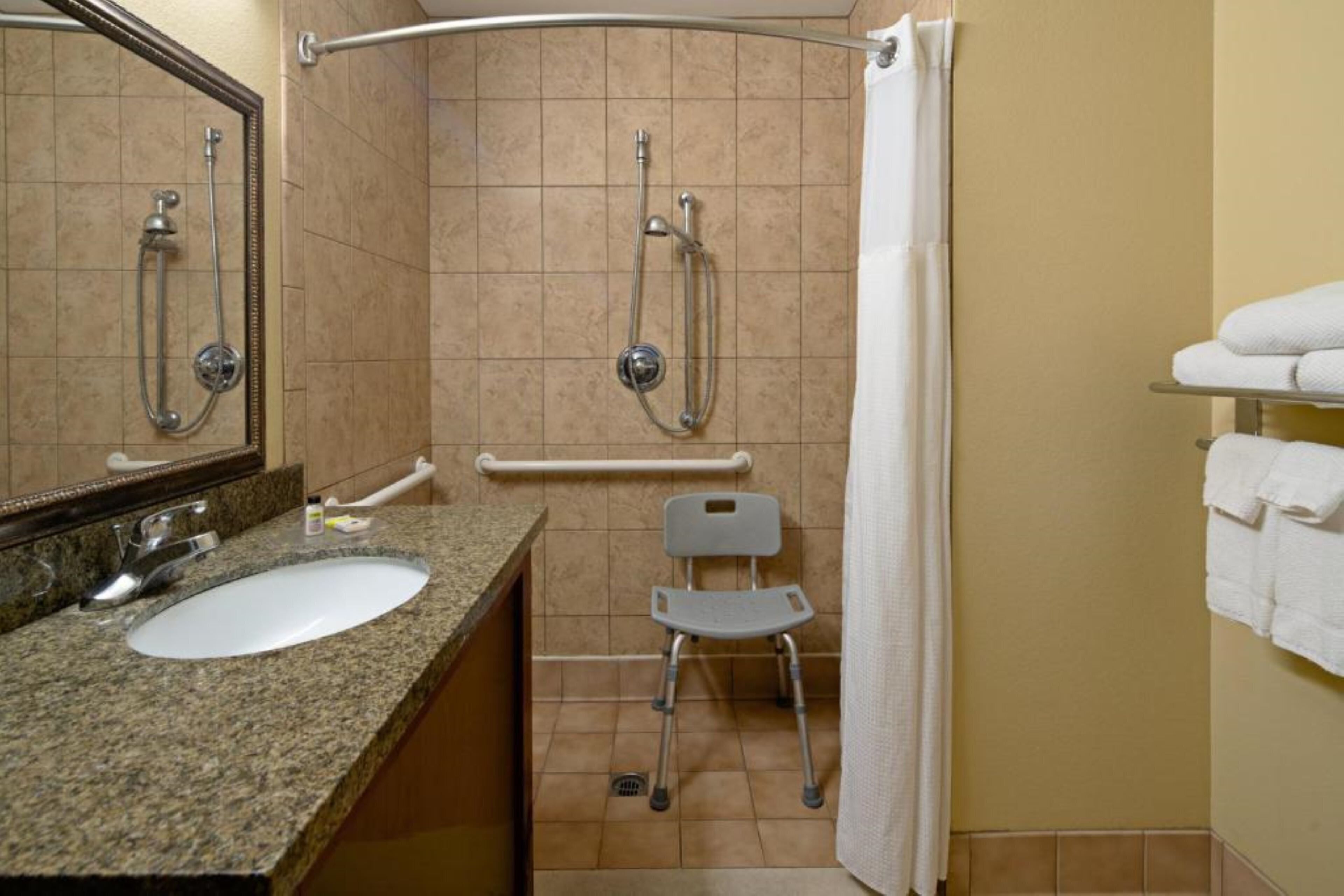 A bathroom with a sink, mirror, shower, grab bar, and a wheelchair.