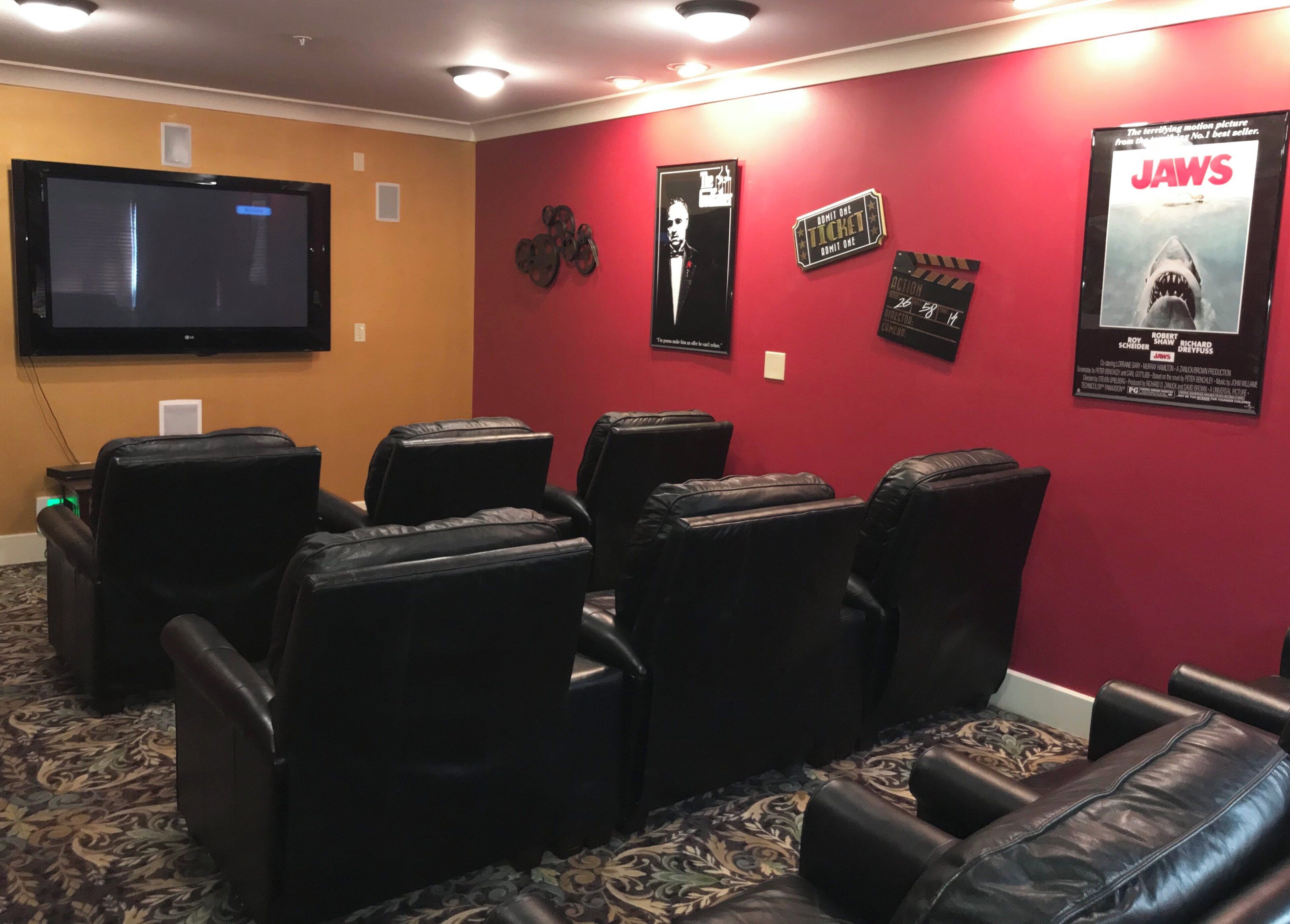 Una sala de cine en casa con butacas reclinables de cuero negro, un televisor de pantalla plana montado en la pared y carteles de películas en la pared.