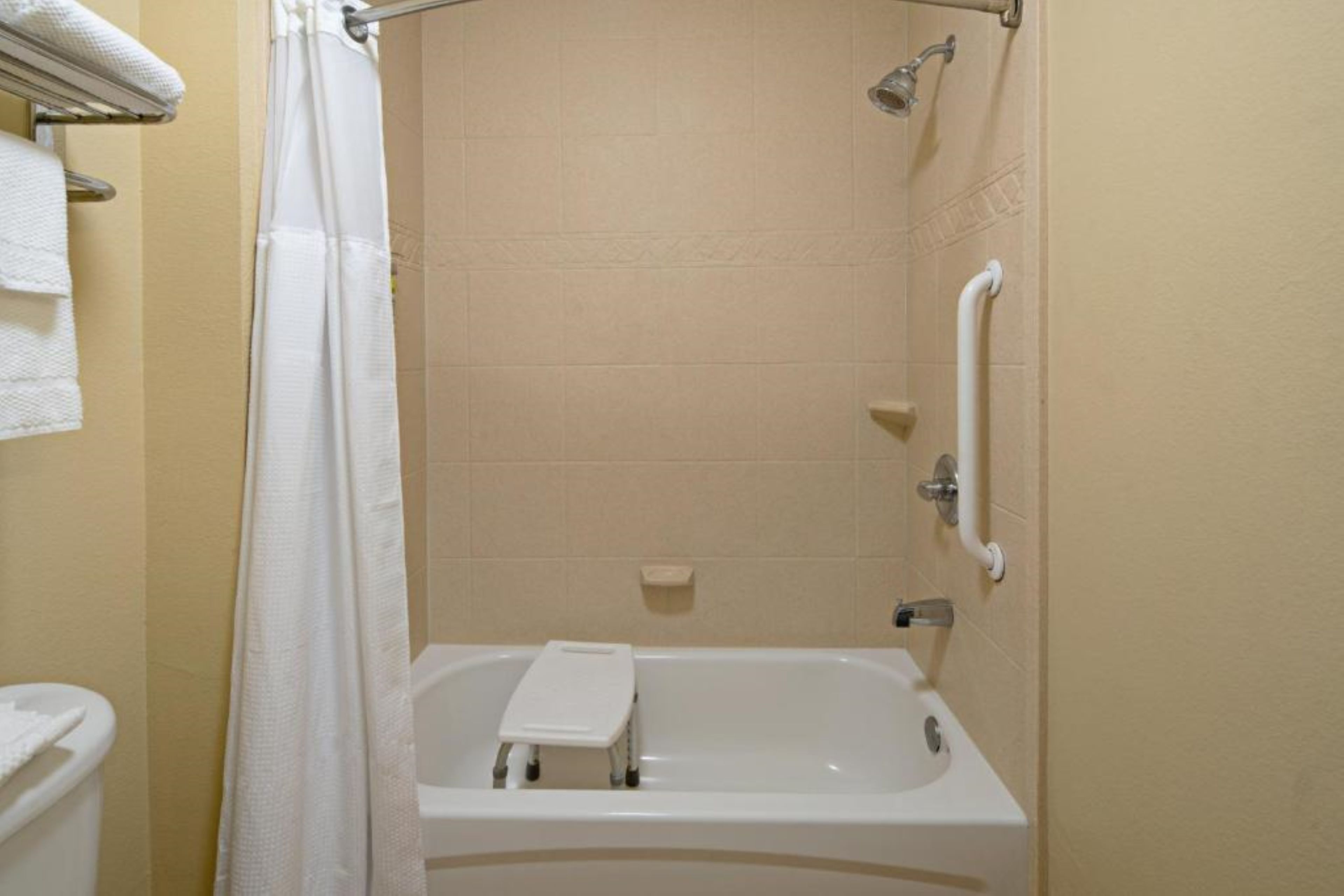 Un baño con bañera, cortina de ducha, barra de apoyo y toallero.