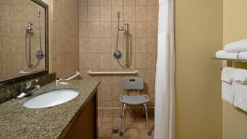 A bathroom with a sink, mirror, shower, grab bar, and a wheelchair.