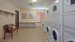 A laundry room with stacked washers and dryers, a bench, and two framed artworks on the wall. - Staybridge Suites Palmdale by IHG (Palmdale)
