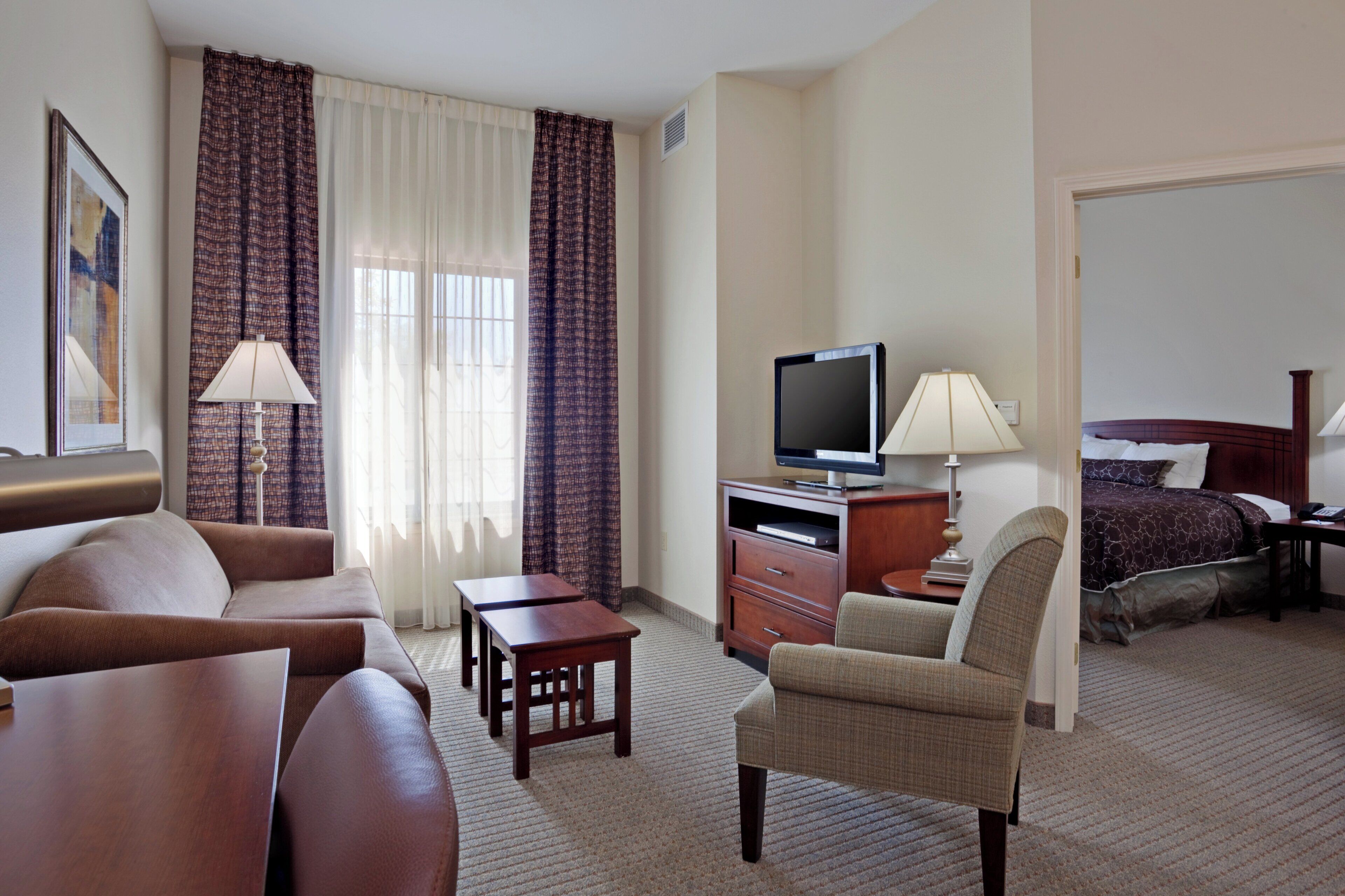 Une chambre d’hôtel équipée d’un canapé, d’un fauteuil, d’une télévision, d’un bureau et d’un lit.