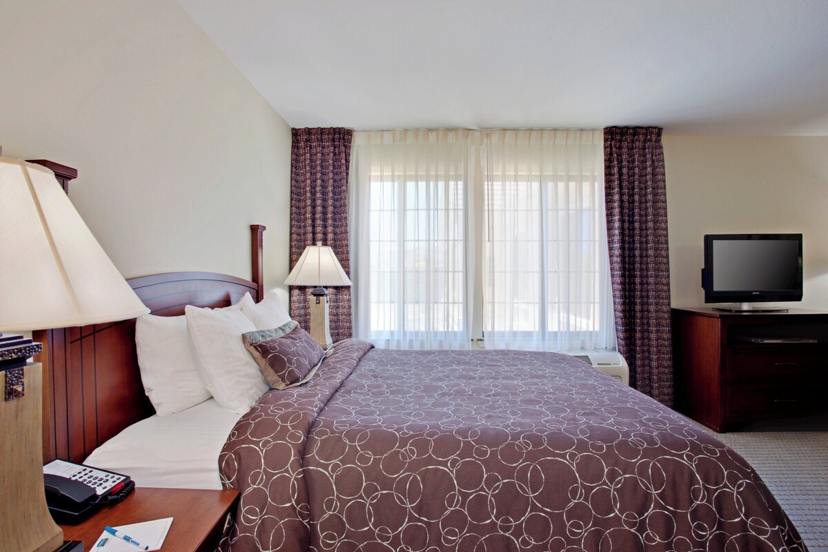 A hotel room with a bed, a television, a desk with a lamp, and a window with curtains.