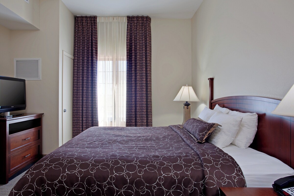 A hotel room with a bed, a television on a dresser, a lamp, and curtains.