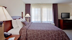 A hotel room with a large bed, a TV, a desk with a lamp, and a window with curtains. - Staybridge Suites Palmdale by IHG (Palmdale)