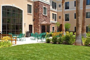 A courtyard with outdoor seating, a stone wall, and palm trees.
