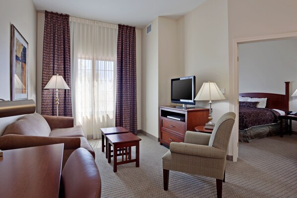 A hotel room with a sofa, armchair, TV, desk, and a bed with a headboard. - Staybridge Suites Palmdale by IHG (Palmdale)