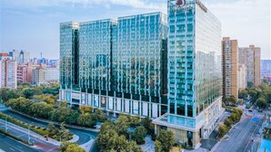 A modern glass building with a prominent logo, surrounded by urban infrastructure and greenery. - DoubleTree by Hilton Beijing (Beijing)