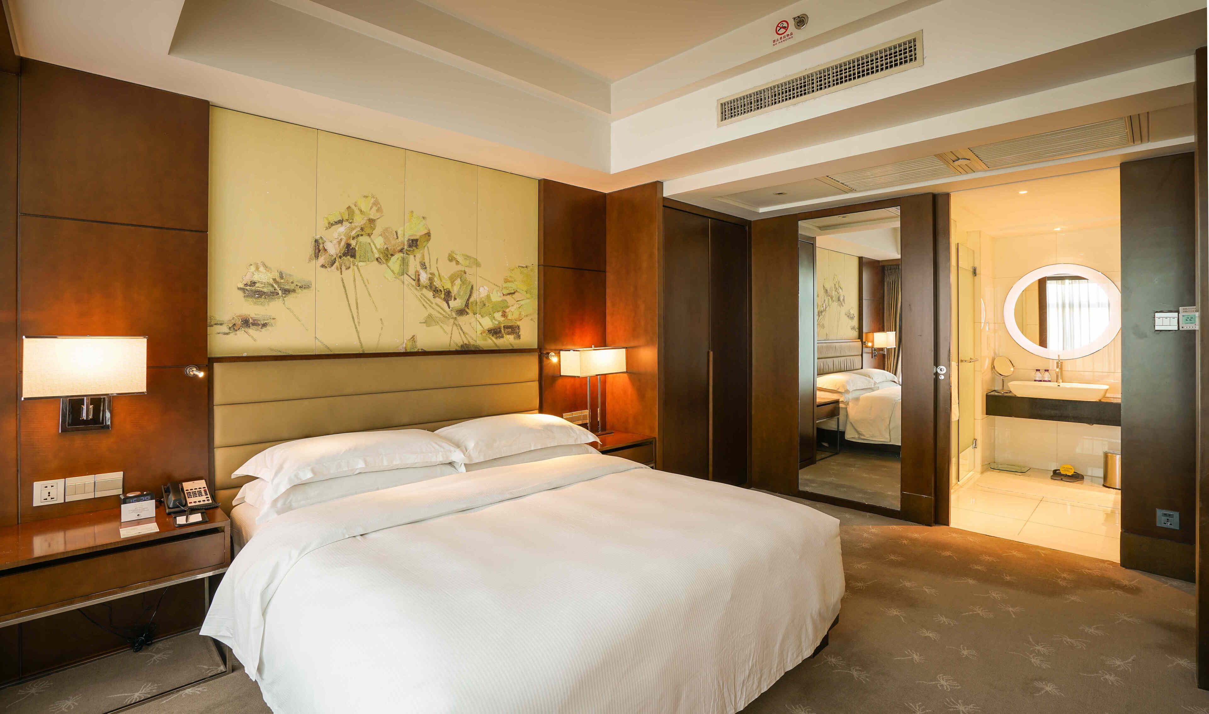 A hotel room with a large bed, bedside lamps, a desk with a phone, and a painting on the wall.