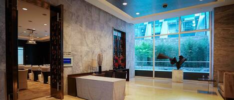 A modern hotel lobby with a reception desk, seating area, and large windows offering a view of the outdoors.