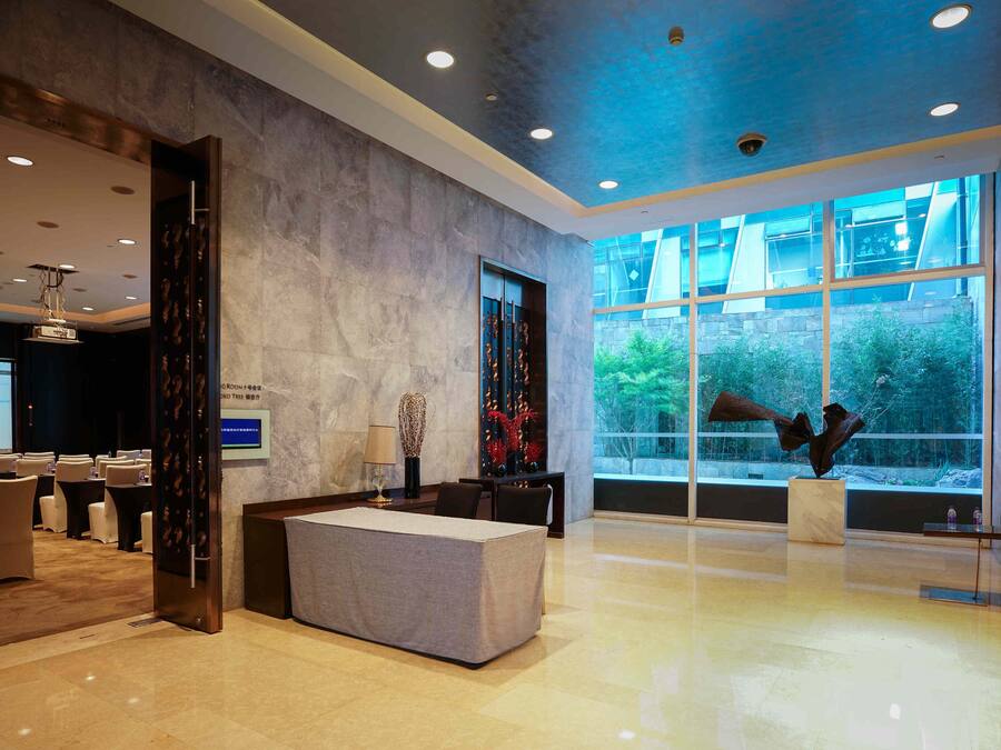 A modern hotel lobby with a reception desk, seating area, and large windows offering a view of the outdoors.