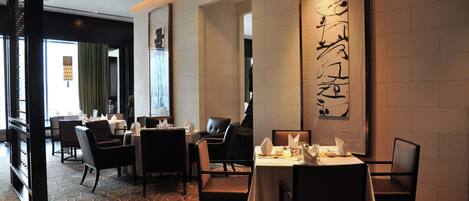 Un restaurante con mesas dispuestas para comer, un letrero vertical grande con texto y una alfombra estampada.