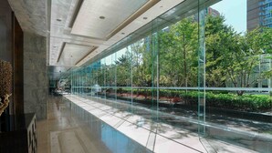 A modern building with a glass corridor, reflecting trees and a water feature. - DoubleTree by Hilton Beijing (Beijing)