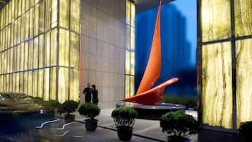 Un vestíbulo moderno con un gran muro de cristal, una escultura naranja singular y plantas en macetas.