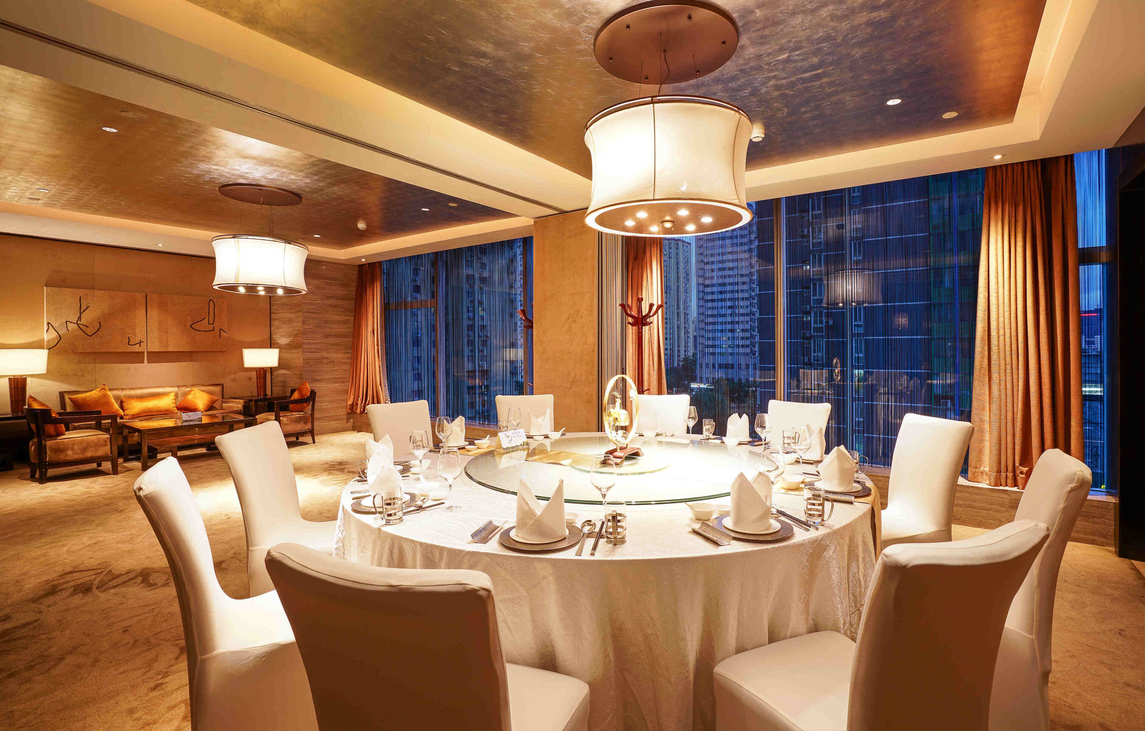 A well-lit, modern dining room with a round table set for six, surrounded by white chairs.