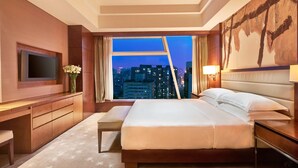 A hotel room with a large bed, a TV, a desk, and a view of the city at dusk. - DoubleTree by Hilton Beijing (Beijing)