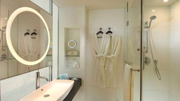 A modern bathroom with a large mirror, a sink, a shower, and two robes hanging on hooks.
