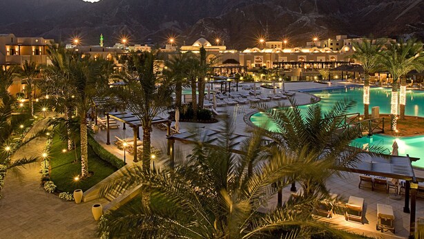 Un resort con piscina, palmeras y montañas al fondo.