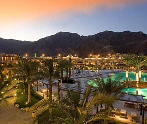 A resort with a swimming pool, palm trees, and a mountain backdrop.