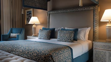 A hotel room with a large bed, a chair, two bedside tables with lamps, and patterned wall and ceiling designs.