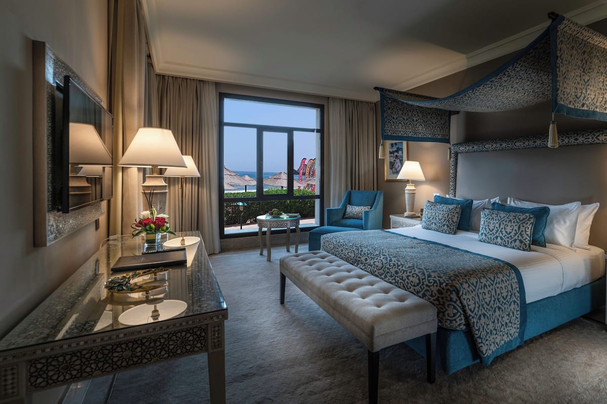 A hotel room with a large bed, two chairs, a desk, and a view of the ocean.
