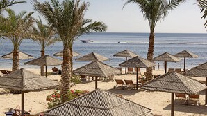 Una playa con sombrillas de paja y sillones reclinables de madera.