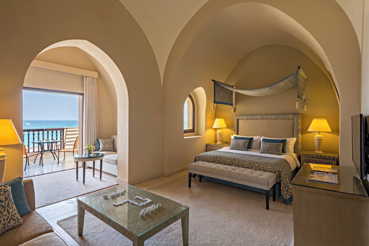A hotel room with a large bed, a balcony with a view, a sitting area with a table, and a TV.