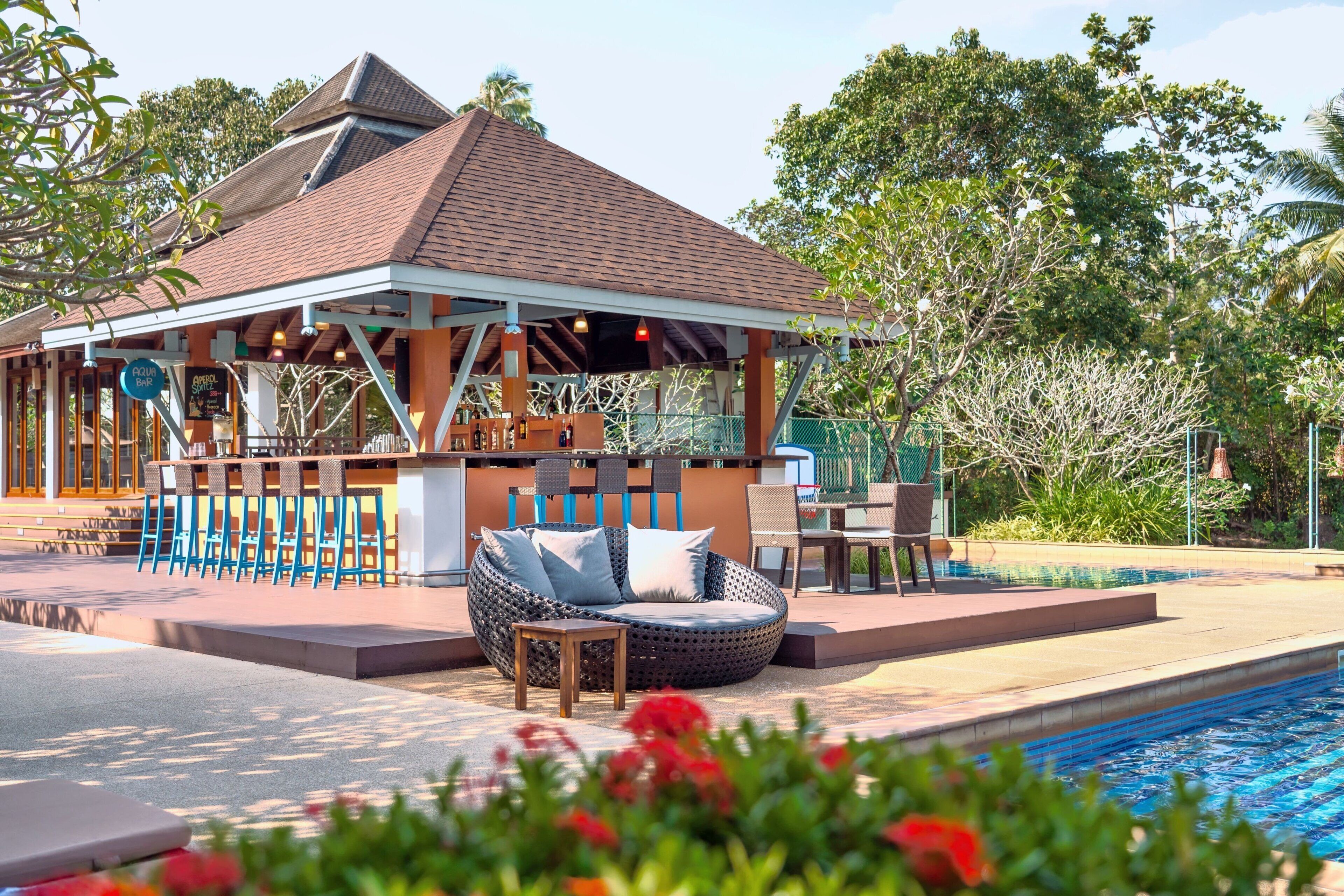 A poolside area with a covered seating area, a bar, and a lounge chair.
