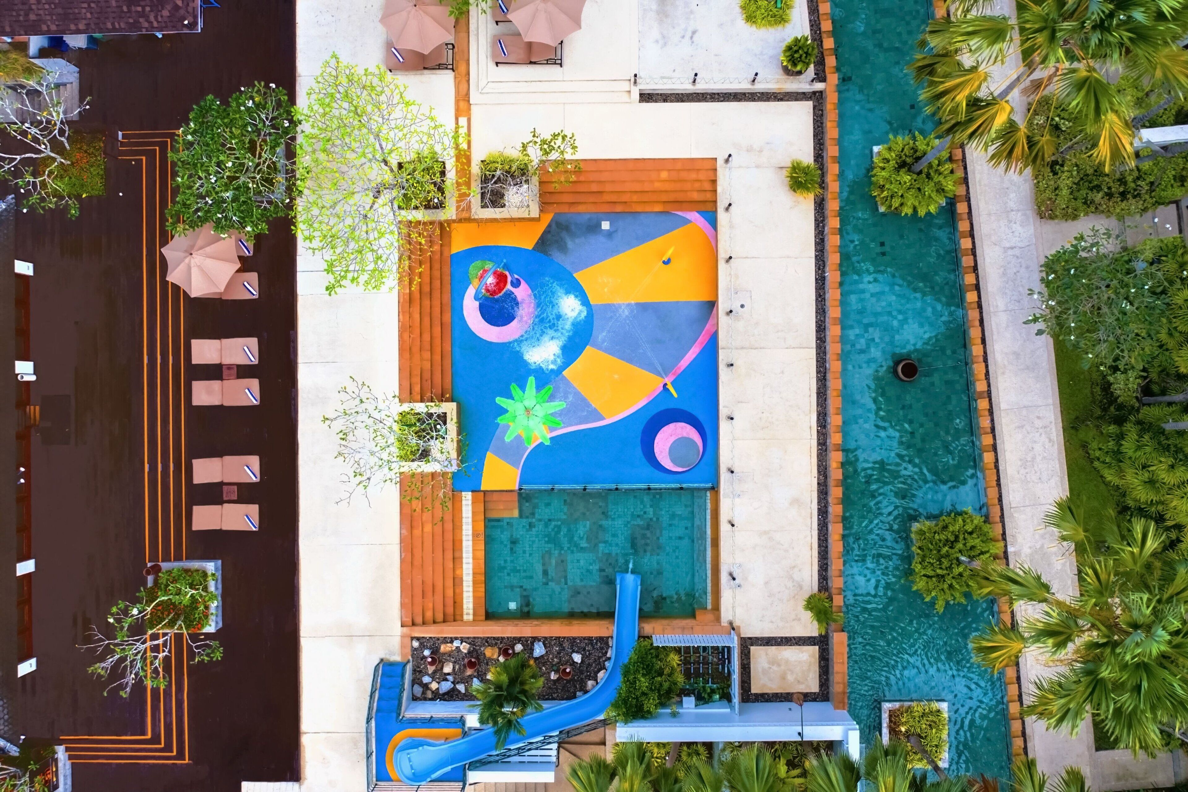 Vista aérea de un hotel con piscina, un mural colorido y mobiliario exterior.