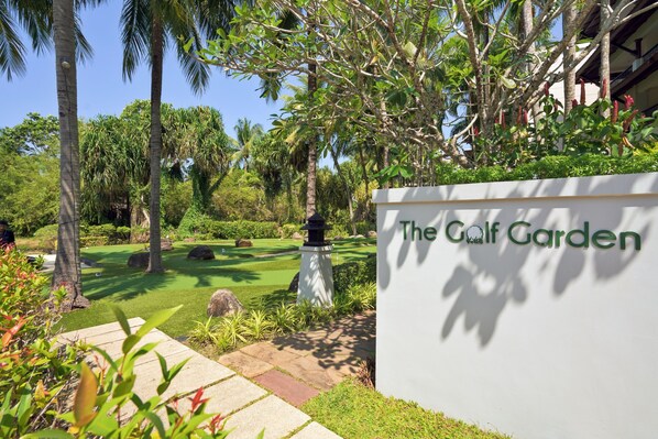 Un campo de golf con un letrero que dice "The Golf Garden", rodeado de exuberante follaje y palmeras.