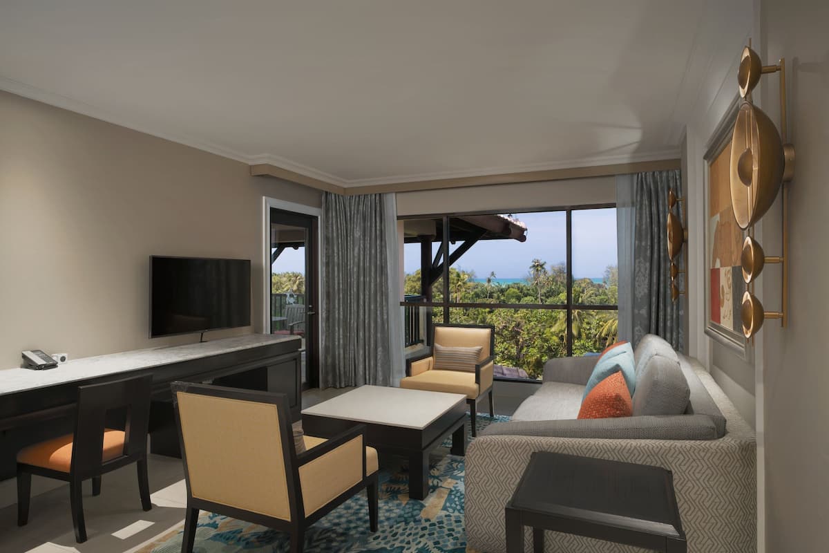 A modern hotel room with a sofa, chairs, a dining table, and a TV.