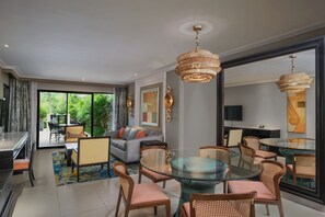A modern living room with a glass dining table, wicker chairs, and a large window offering a view of the outdoors. - Marriott’s Mai Khao Resort - Phuket (Mai Khao)