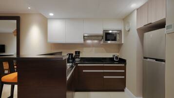 A compact kitchen with dark wooden cabinets, a stainless steel refrigerator, a microwave, and a coffee maker.