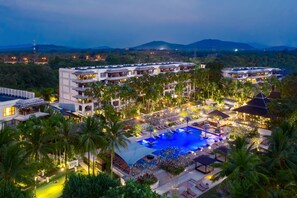 Un resort con varias edificaciones, una gran piscina y follaje circundante.