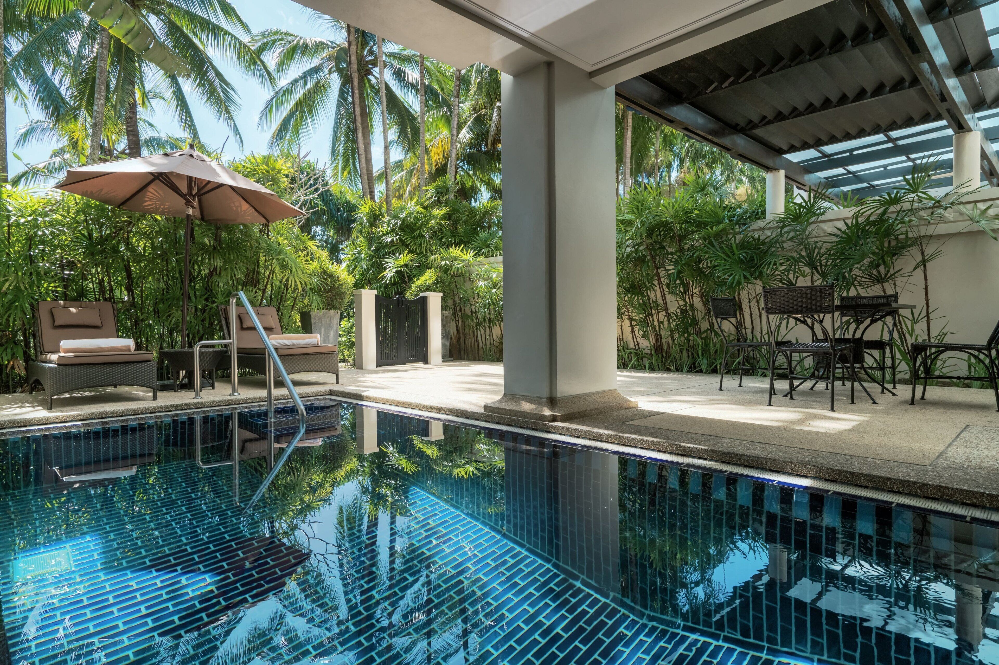 A clear blue pool with a tiled deck, lounge chairs, and umbrellas.