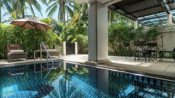 A clear blue pool with a tiled deck, lounge chairs, and umbrellas.