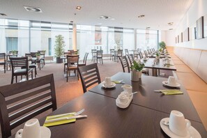A spacious dining area with multiple tables set for breakfast, featuring white cups and plates, and potted plants.