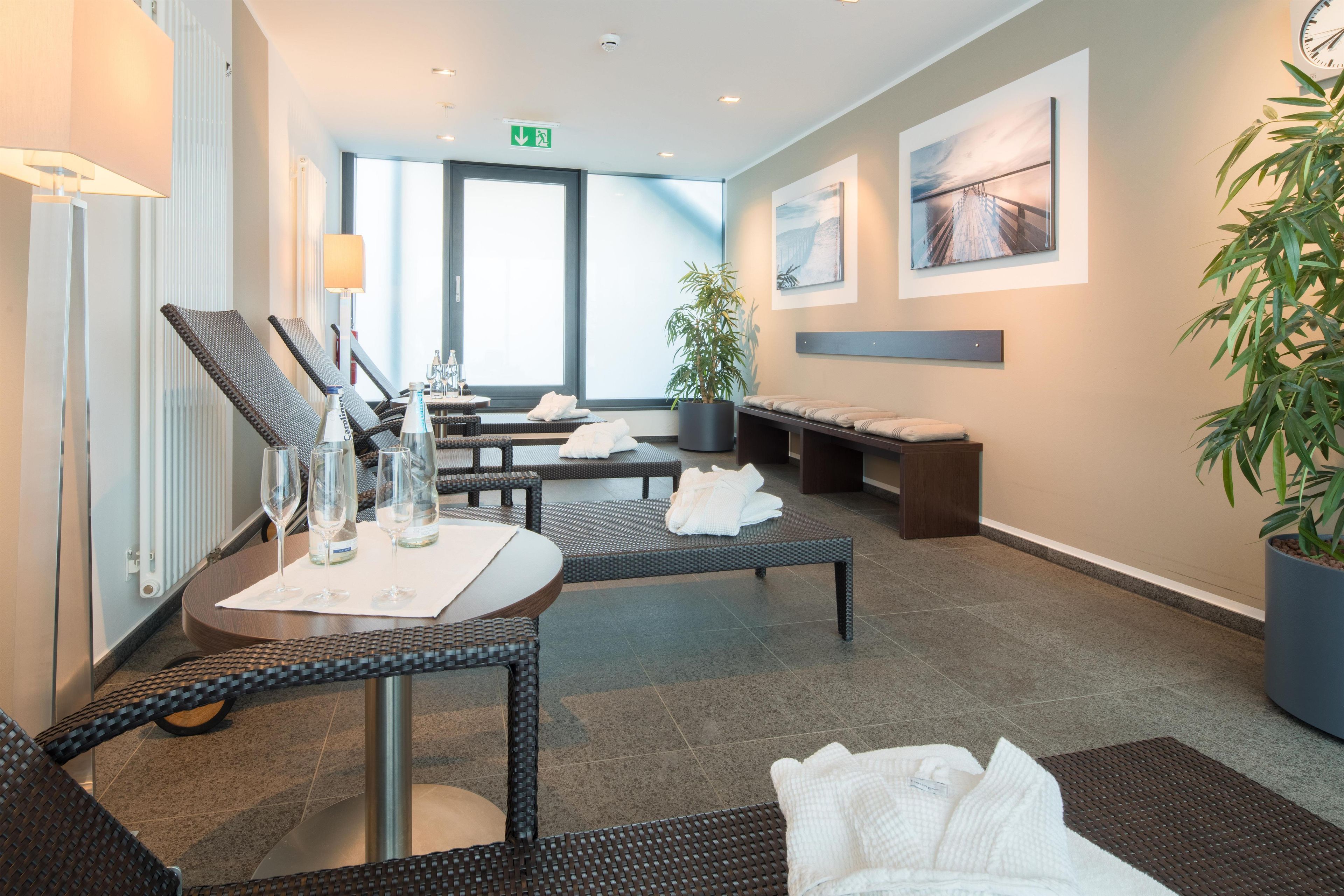 Ein moderner Wellnessbereich mit Korbmöbeln, einem Massagetisch und einer großen Topfpflanze.