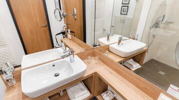Un baño moderno con dos lavamanos, un espejo, un secador de pelo y una ducha.