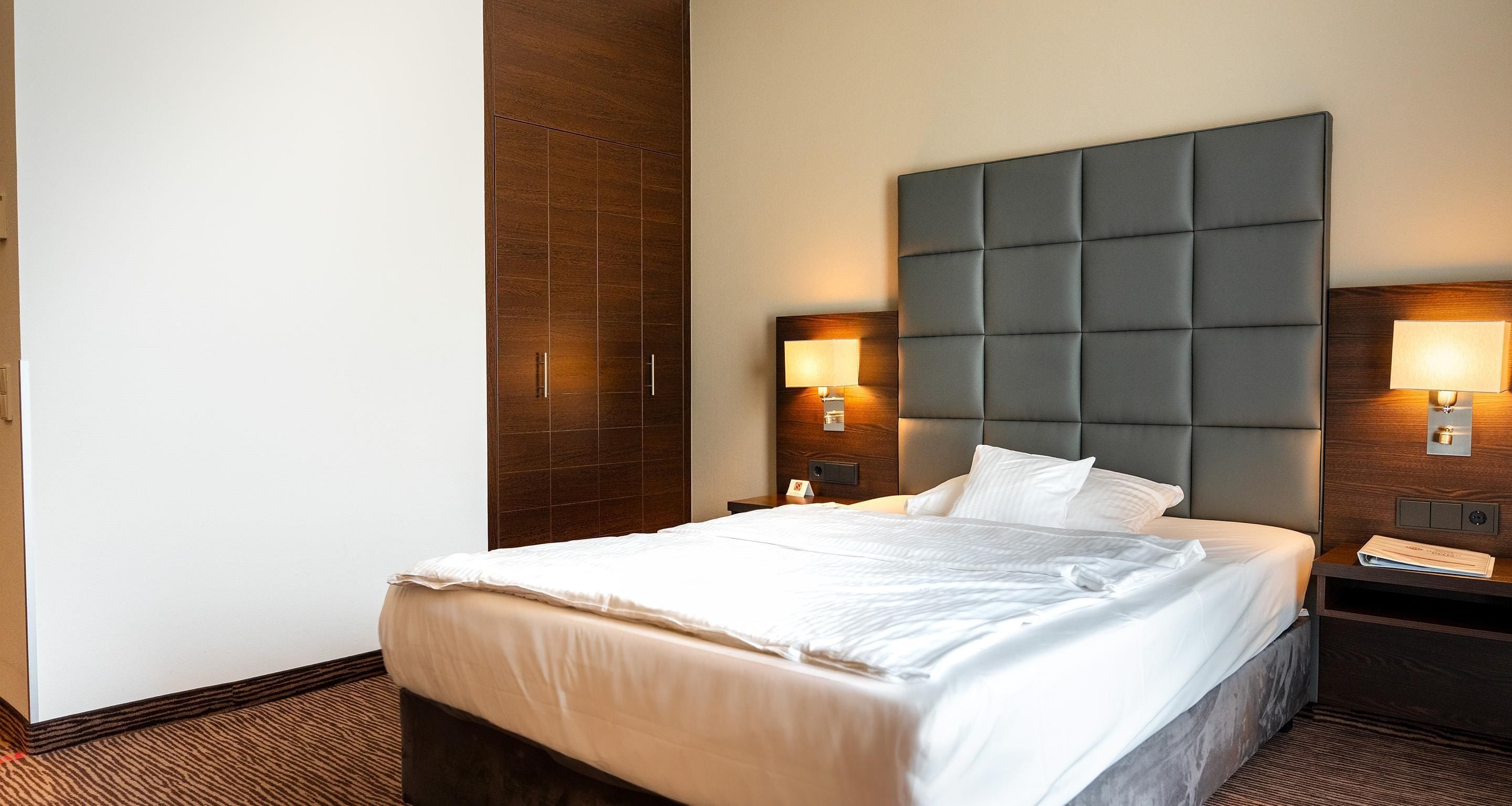 A hotel room with a large bed, wooden headboard, two bedside tables with lamps, and a nightstand.